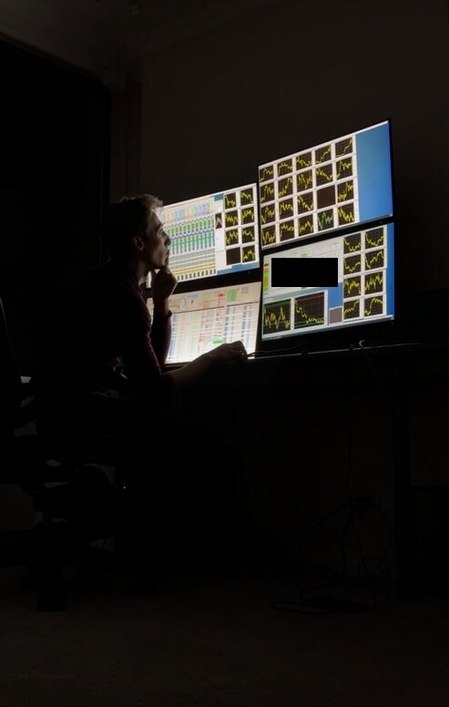 At a trading desk in a dark room, facing a wall of monitors